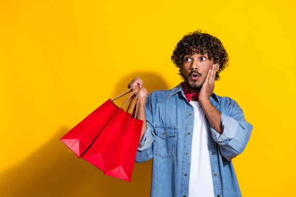 照片上漂亮的年轻男性购物袋看起来很神奇，空着时尚的牛仔服装，红色围巾孤立在黄色背景上图片下载