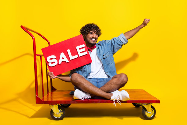 漂亮的年轻男性出货推车的全尺寸照片持有销售盘穿着时尚的牛仔服装红色围巾孤立的黄色背景图片下载