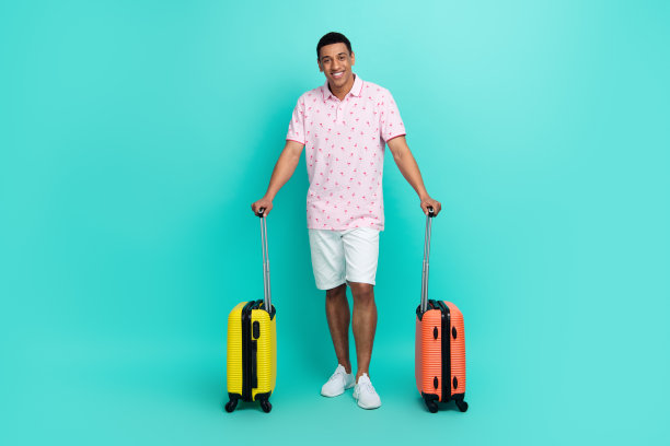 全长照片的好心情男人穿粉红色polo白色短裤拿行李准备度假孤立的绿松石色背景图片下载