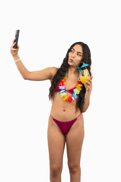 穿着比基尼的拉丁女孩在白色背景下享受夏日鸡尾酒的同时自拍图片下载
