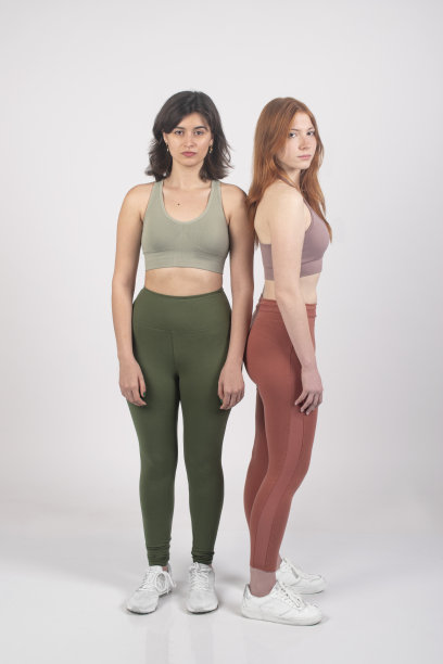 垂直框架的两个女人在运动服瑜伽站背靠背与一个自信的姿势在一个简单的背景。图片下载