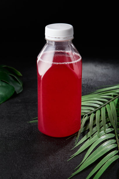 浆果饮料在黑色背景与叶子取出瓶。模拟饮料在最小的概念与黑色背景和棕榈叶。瓶装冷饮，用于展示包装。浆果酒。图片下载