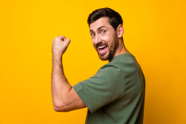 照片中强壮兴奋的男子身穿卡其色t恤，高举拳头，露出肌肉孤立的黄色背景图片下载
