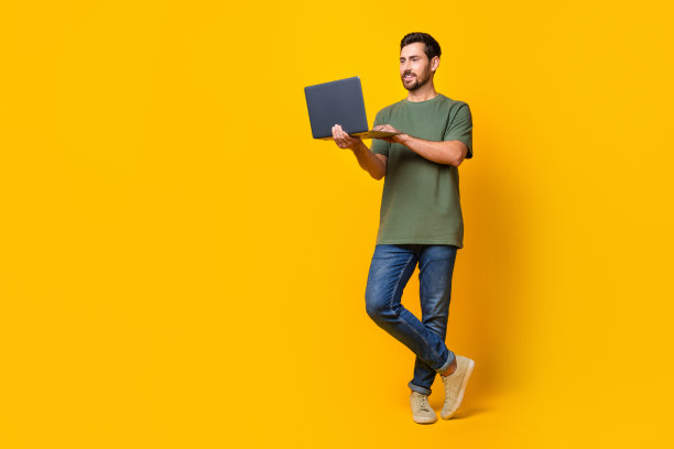 漂亮的年轻男性手持上网本的电子商务营销人员的全身照片，穿着时尚的卡其色服装，孤立在黄色背景上图片下载