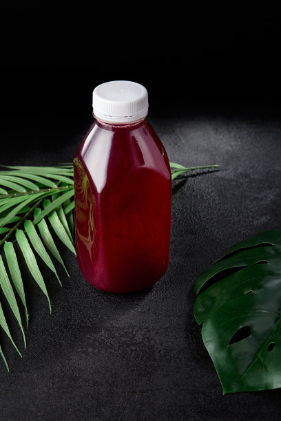 浆果饮料在黑色背景与叶子取出瓶。模拟饮料在最小的概念与黑色背景和棕榈叶。瓶装冷饮，用于展示包装。浆果酒。图片下载