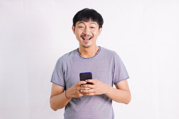 一个年轻人的全景照片，手里拿着智能手机，在线聊天，浏览互联网，对智能手机感到震惊，站在孤立的白色背景上图片下载