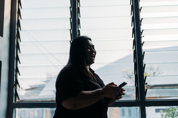 年轻女商人的剪影站在窗口与手机在启动办公室-库存照片图片下载