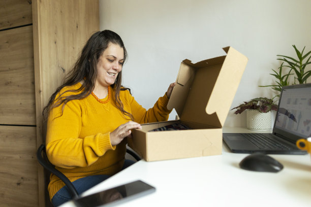 在家网购，美女打开网购收到的包裹。穿着舒适的黄色毛衣。库存图片图片下载