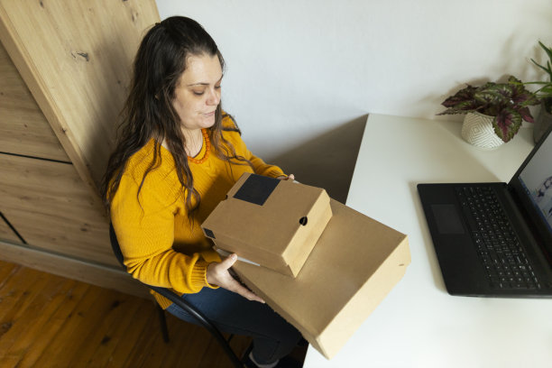 在家网购，美女打开网购收到的包裹。穿着舒适的黄色毛衣。库存图片图片下载