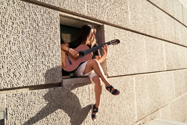 一个女人坐在墙上的凹槽里弹吉他，文字的复制空间。极简主义的照片。图片下载