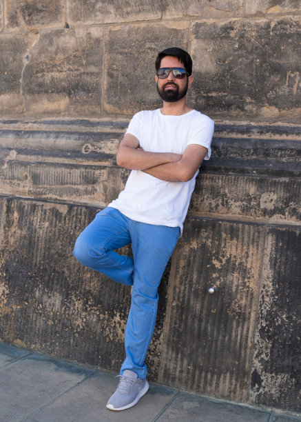 一个留着黑胡子、穿着浅色衣服的现代时尚的巴基斯坦男人站在石墙旁边图片下载