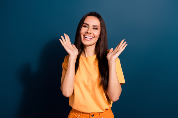 照片中乐观积极的女性，留着长发，穿着黄色t恤，在深蓝色的背景下举起手掌图片下载