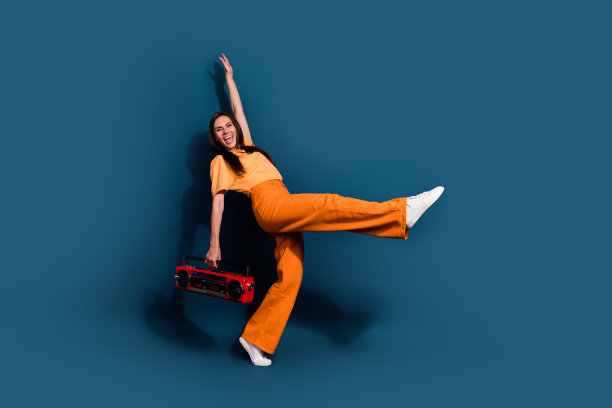 全身照片的女人穿着橙色t恤和裤子，手拿dj小音箱从80年代孤立的深蓝色背景图片下载