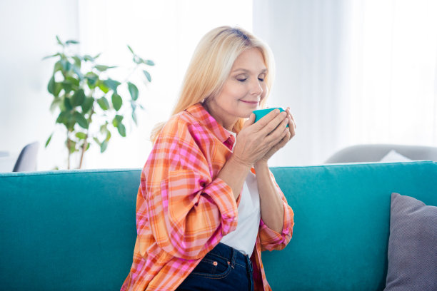 照片中的老太太坐在舒适的沙发上，闻着屋里热咖啡的香味图片下载