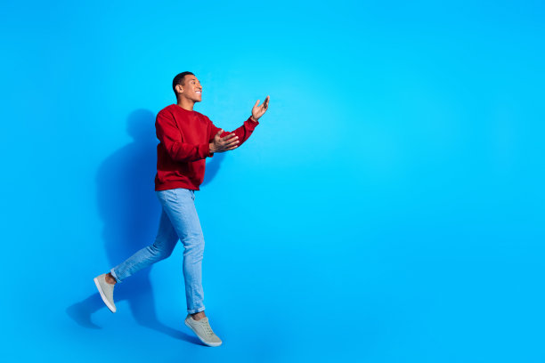 欢快的年轻人的全尺寸个人资料照片跳跑手臂抓住空白空间孤立的蓝色背景图片下载