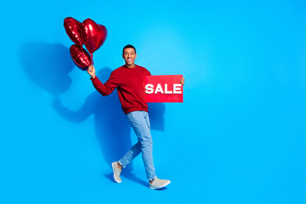 欢乐的人的全尺寸侧面照片拿着销售海报心形气球在蓝色背景上走空图片下载