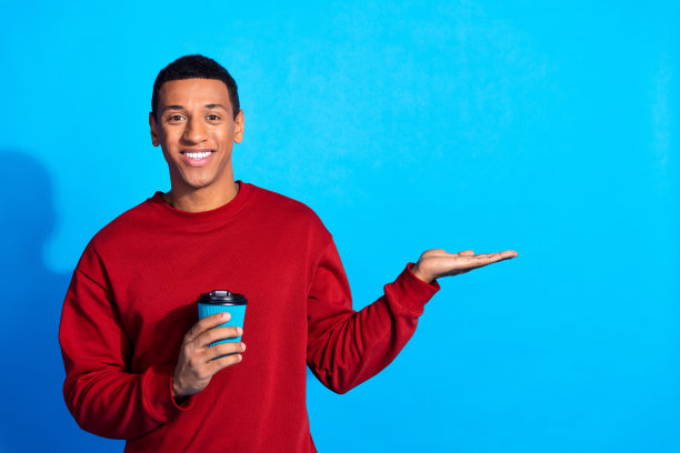积极的年轻人的照片，露齿微笑，拿着咖啡杯，手臂手掌，在蓝色的背景上展示空白的空间图片下载