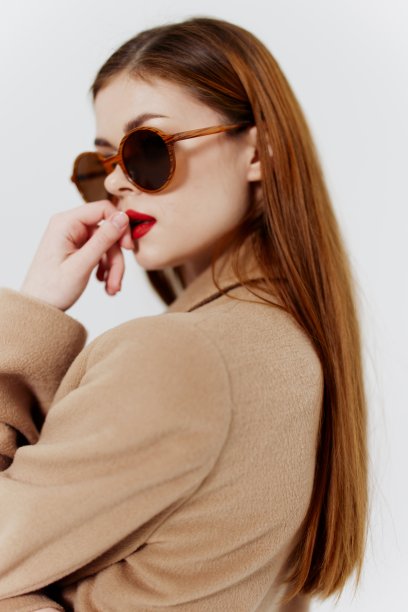 一位时尚的年轻女子戴着眼镜，穿着米色外套，在白色背景上穿着设计师设计的服装，在摄影棚拍摄目录照片图片下载