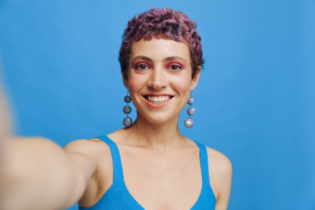 年轻的运动女性时尚博主在蓝色单色背景下，用手机拍了一张自己穿着蓝色运动服微笑着看着相机的照片图片下载