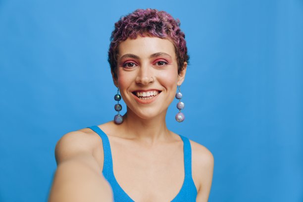 年轻的运动女性时尚博主在蓝色单色背景下，用手机拍了一张自己穿着蓝色运动服微笑着看着相机的照片图片下载