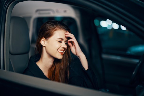一个时髦、奢华的女人晚上坐在一辆黑色轿车的副驾驶座上，闭着眼睛，用手捂着脸，开心地笑着。近距离水平照片图片下载