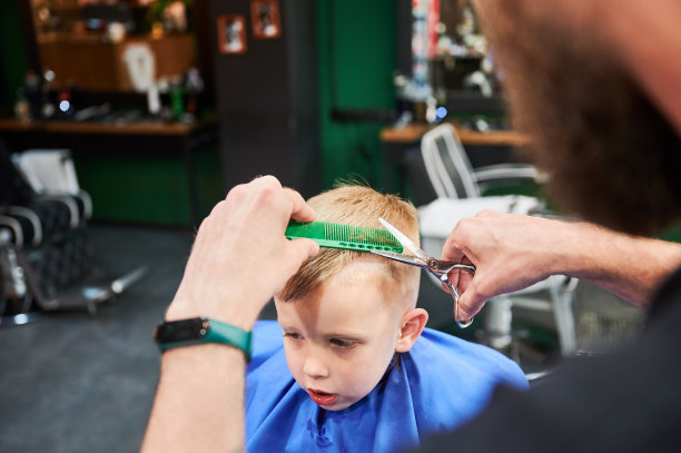 背后的理发师剪小男孩的头发。图片下载