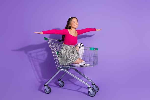 时髦兴奋的女士穿着上身飞臂两侧骑超市手推车空的空间孤立的紫色背景的全身照片图片下载
