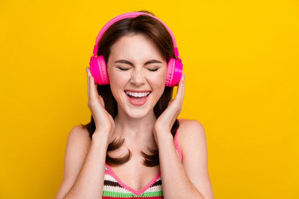 照片中，开朗可爱的女孩穿着条纹顶触式耳机，在明亮的黄色背景下听摇滚播放列表图片下载
