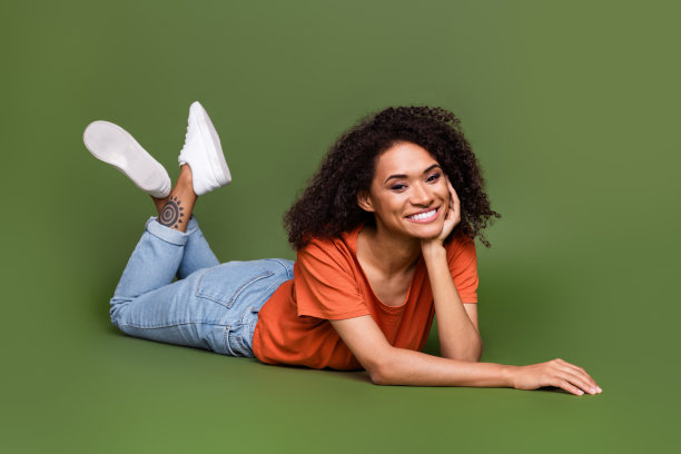 全身照片梦幻闪亮的女人穿橙色t恤手臂脸颊躺在地板孤立的绿色背景图片下载