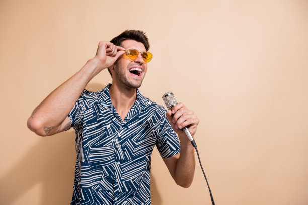 照片中开朗有吸引力的酷男人穿着时髦的衣服，在米色背景上唱歌，看起来很空旷图片下载