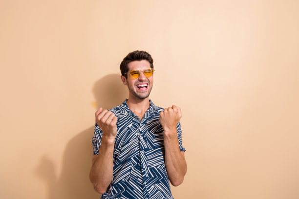 照片积极喜出望外的男人穿着时尚的衣服，戴着太阳镜，听着音乐，在米色的背景上享受周末图片下载