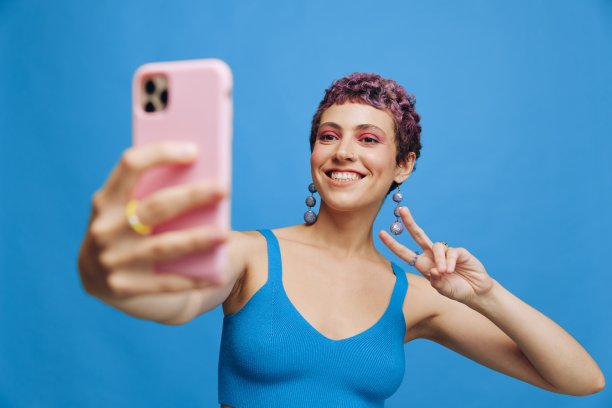 年轻的运动女性时尚博主用手机拍了一张自己穿着蓝色运动服的照片，在蓝色单色背景上微笑着露出舌头图片下载