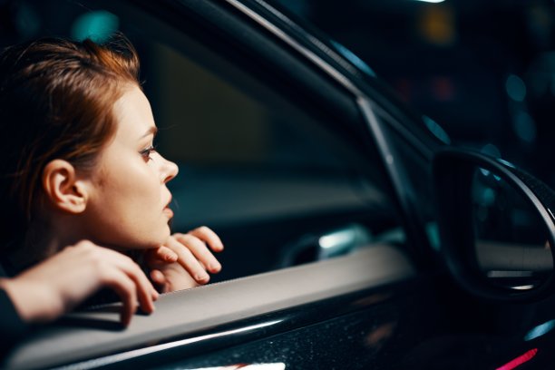 这是一张夜间从侧面拍摄的近距离横向照片，一位妇女坐在一辆黑色轿车里，看着窗外的侧视镜图片下载