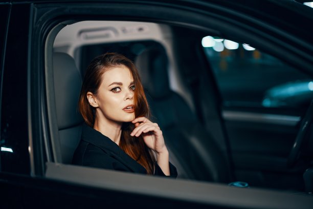 从侧面的横向照片，在晚上，一个女人坐在一辆黑色的车里，若有所思地看着相机，把手放在脸附近，把车停在停车场图片下载