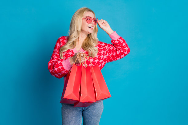 照片可爱的女人穿针织开襟羊毛衫触摸眼镜看促销空的空间持有新衣服的袋子孤立的蓝色背景图片下载
