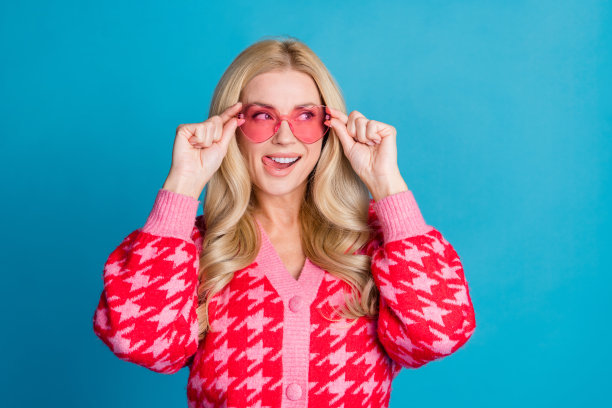 照片中的女人波浪的头发，穿着针织开衫，触摸眼镜，看着销售空白的空间，舔嘴唇孤立的蓝色背景图片下载