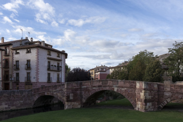 多云的天空下，石桥、绿草和建筑的美景图片下载