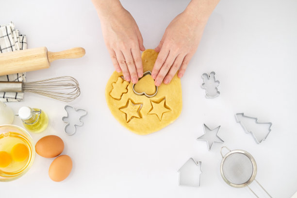 裁剪后的图片，手在厨房烘烤时切面团饼干。制作自制饼干。桌上放着面团和一套饼干模具，还有其他厨房设备。图片下载