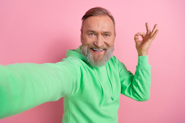 照片正面的酷男人穿着绿色运动衫，显示ok的标志，录制视频视频博客孤立的粉红色背景图片下载