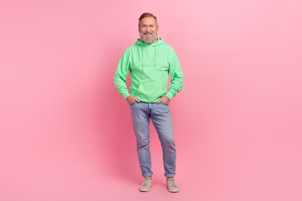 漂亮的退休男性双手口袋牛仔裤模特购物穿着时尚的绿色服装孤立的粉红色背景的全身照片图片下载