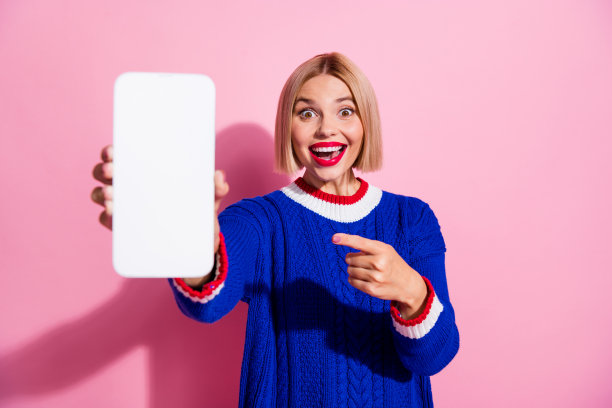 年轻惊奇的女孩蓝色时髦套头衫的照片推荐访问这个网站点指手机显示孤立的粉红色背景图片下载