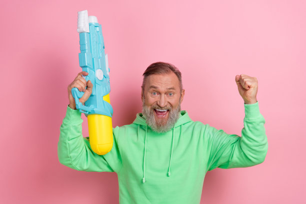 照片的幸运兴奋的男子穿着绿色运动衫赢得水上射击游戏孤立的粉红色背景图片下载