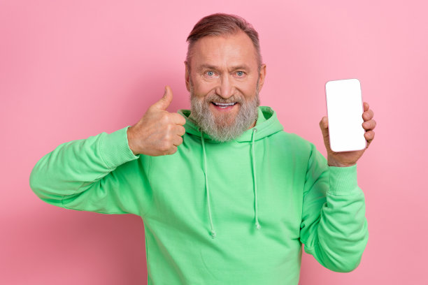 照片的好心情自信的家伙穿着绿色卫衣显示大拇指现代设备空白空间孤立的粉红色背景图片下载