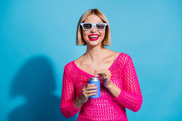 迷人的年轻女子的照片肖像喝汽水可以3d眼镜穿时髦的粉红色针织品衣服孤立的蓝色背景图片下载