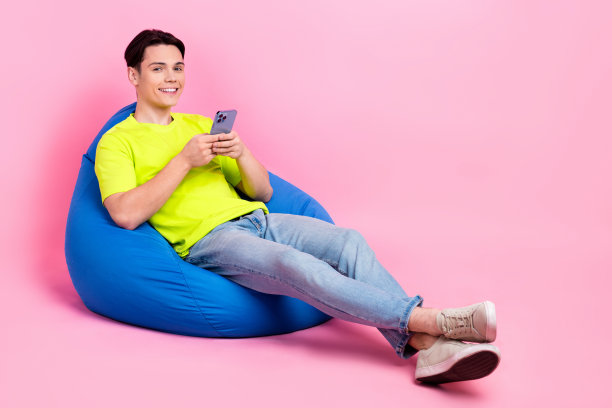 正面的全长照片酷男人穿着t恤坐在豆袋聊天现代装置空旷的空间孤立的粉红色背景图片下载