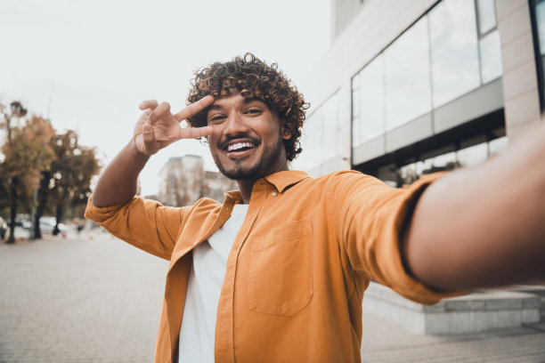 照片积极的好高兴的男人穿时髦的衣服有乐趣直播制作视频自拍秀v-sign图片下载