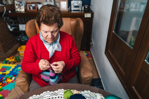 年长的妇女在家中沙发上用针和彩色羊毛缝纫的横向照片图片下载