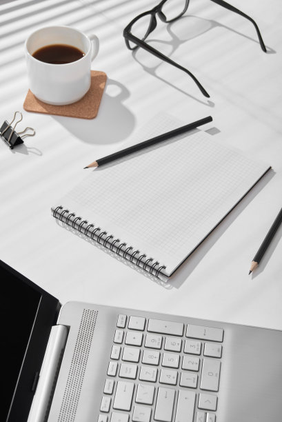 在一个阳光明媚的日子里，在铅笔和笔记本电脑旁边的桌子上放着一个记笔记的记事本。图片下载