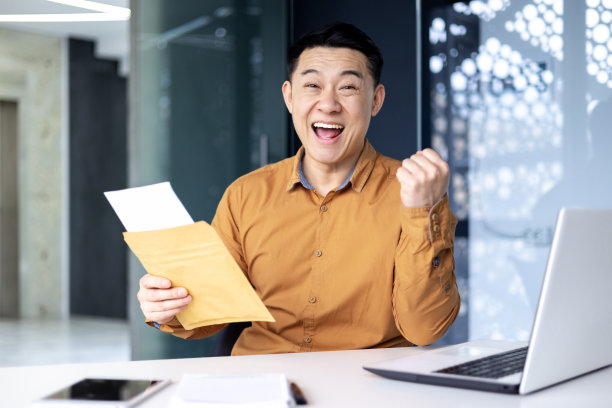 亚洲商人对签订的合同感到高兴，坐在办公室的桌子旁，手里拿着文件，满意地举起手，与文件一起工作，事业有成图片下载