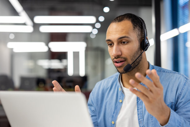 严肃的年轻西班牙人戴着耳机坐在办公室的桌子上进行视频通话。特写照片图片下载